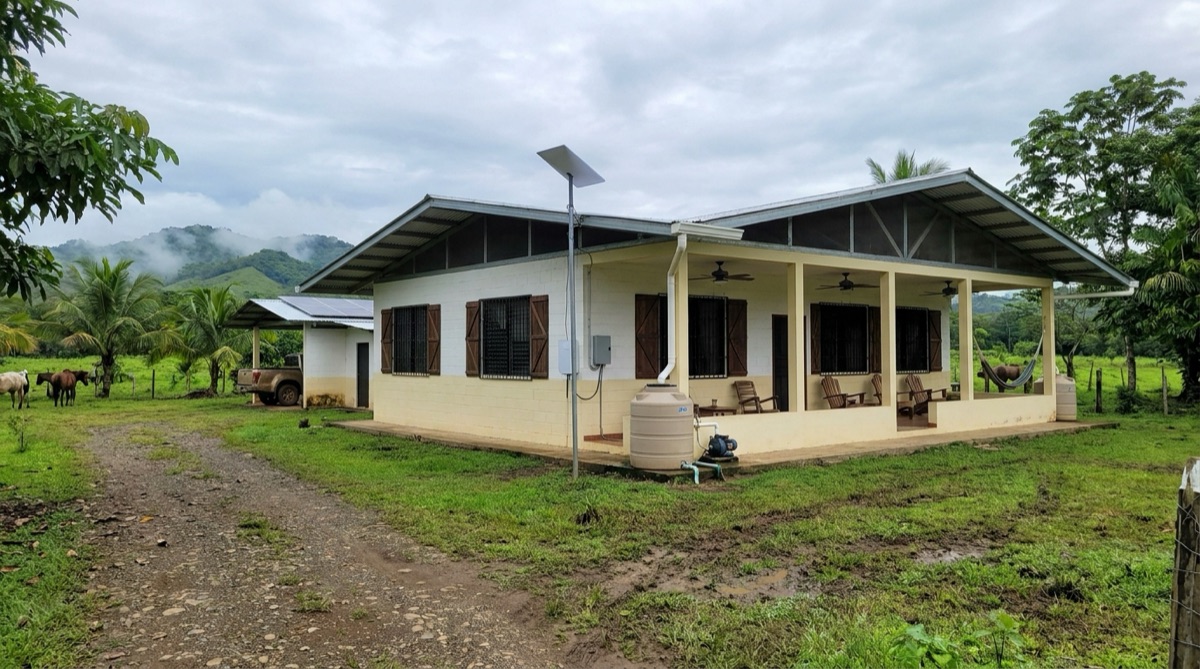 The outside of Stefan's Panamanian house, a modest finca with a covered terrace, parked vehicle, horses in the pasture, and misty hills behind it.